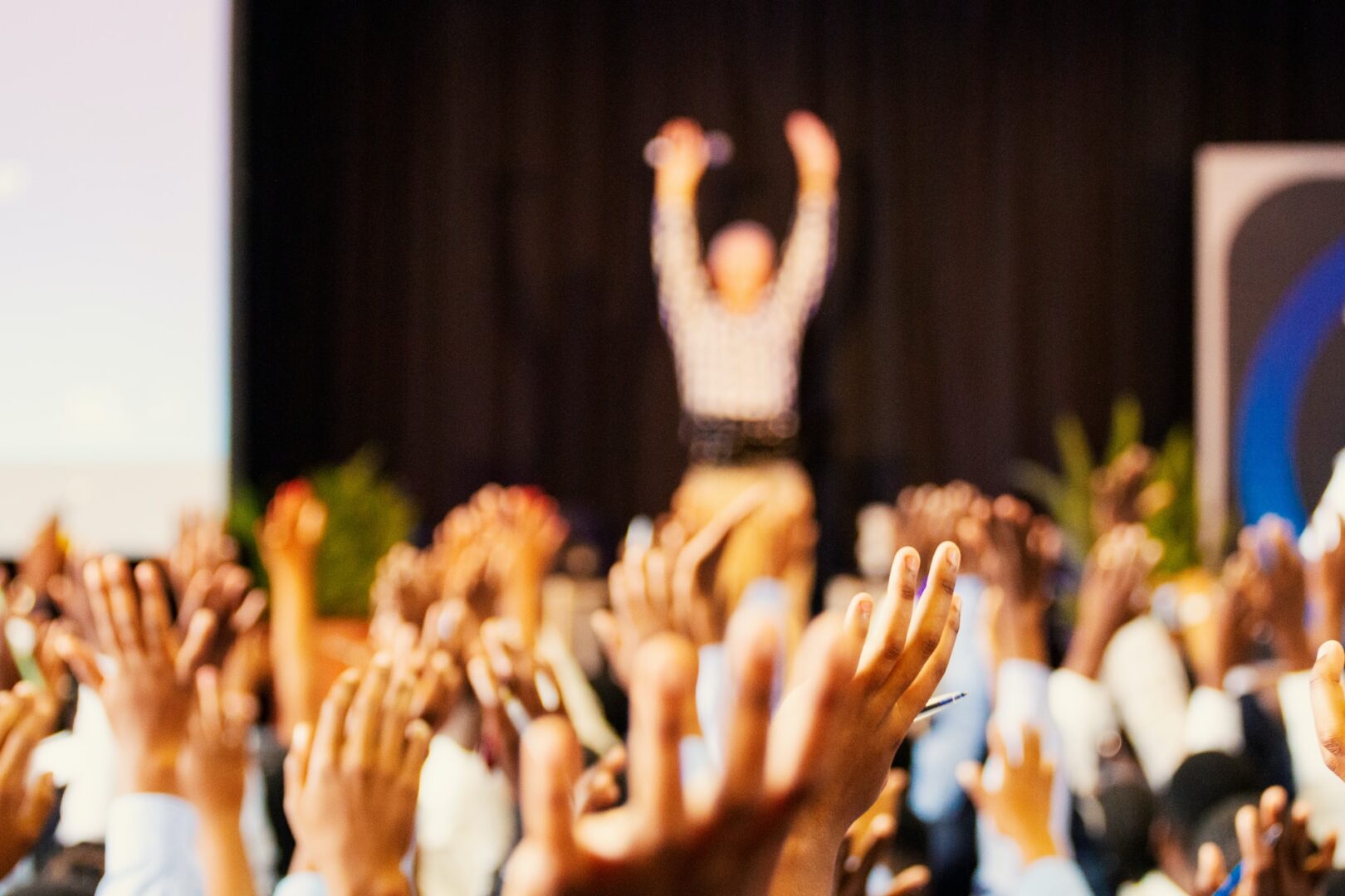 A crowd of people raising their hands in front of a stage.